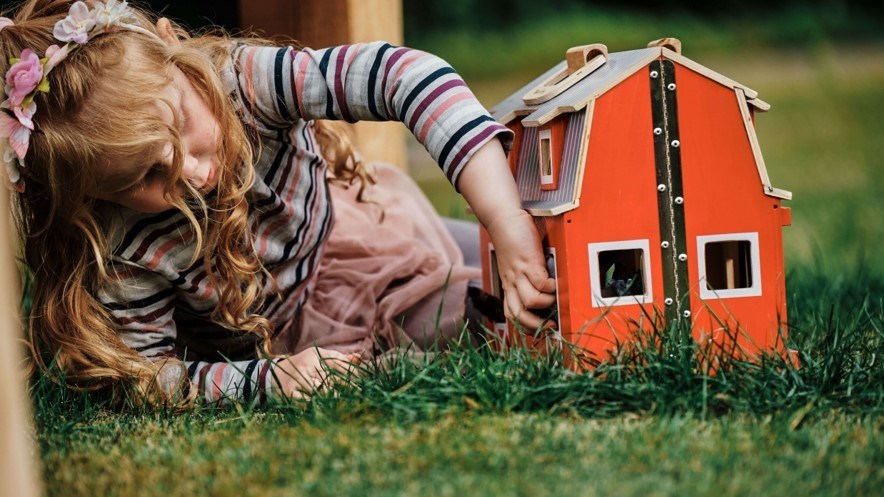 ett barn ligger i gräset och leker med ett dockhus